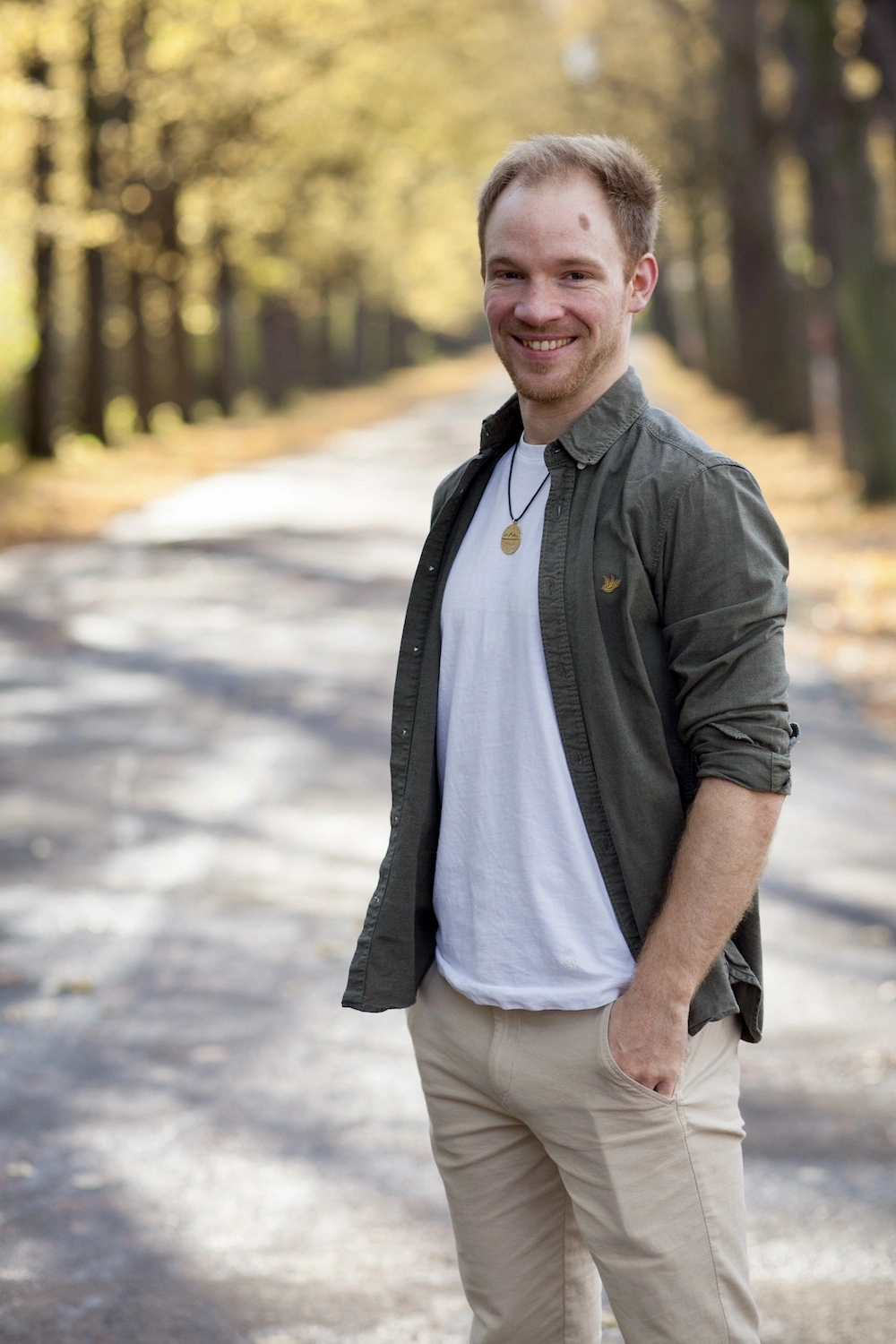 Ein lächelnder Mann mit einem verschwommenen Wald im Hintergrund.